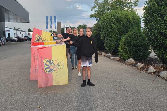Gruppierung von Personen mit Flaggen auf einem gepflasterten Weg bei bewölktem Himmel.